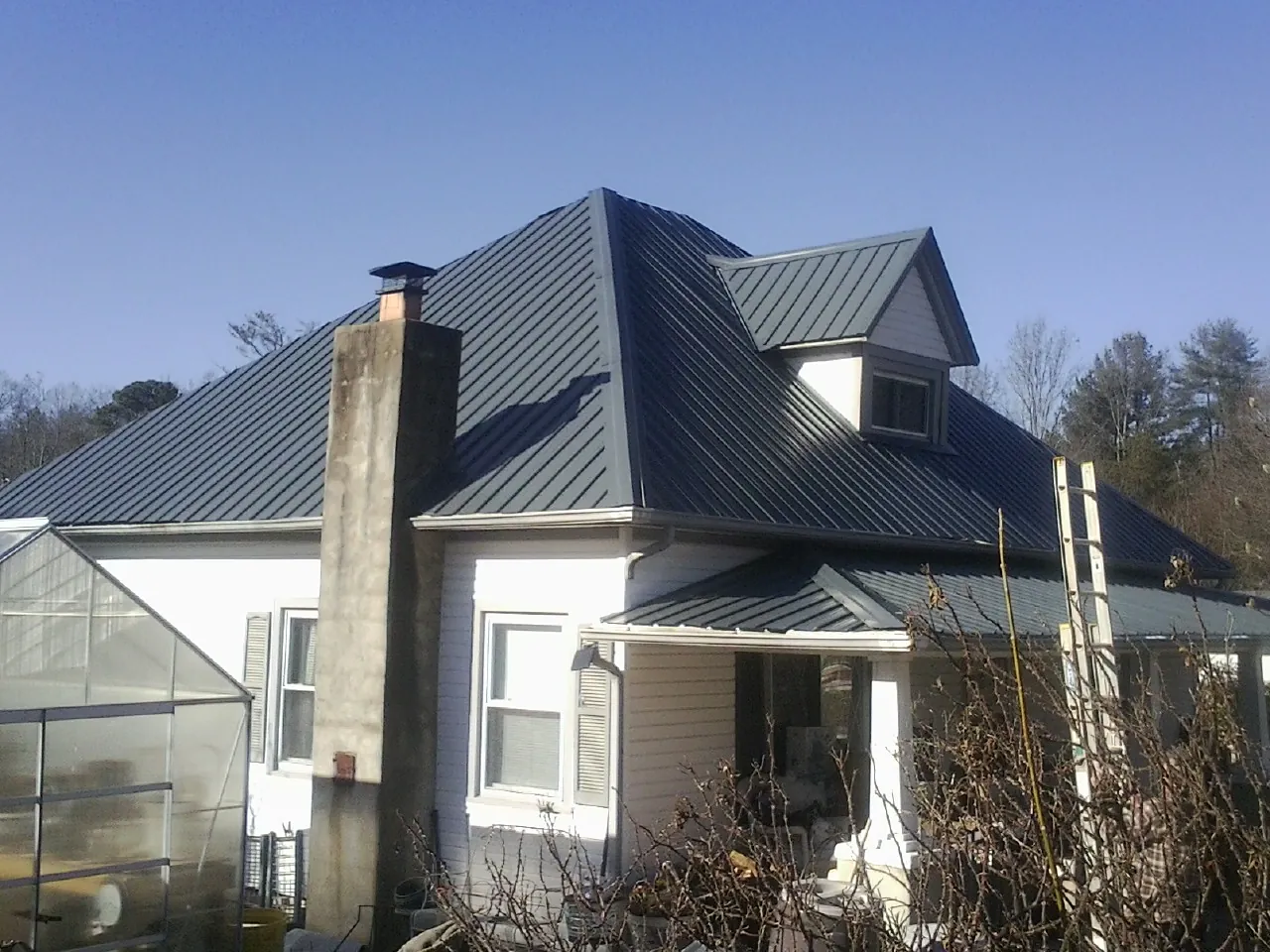 Dark blue standing seam metal roof on a white farmhouse with dormer — Slate & Tile Roof Repair by Roofing Brothers in Brazil
