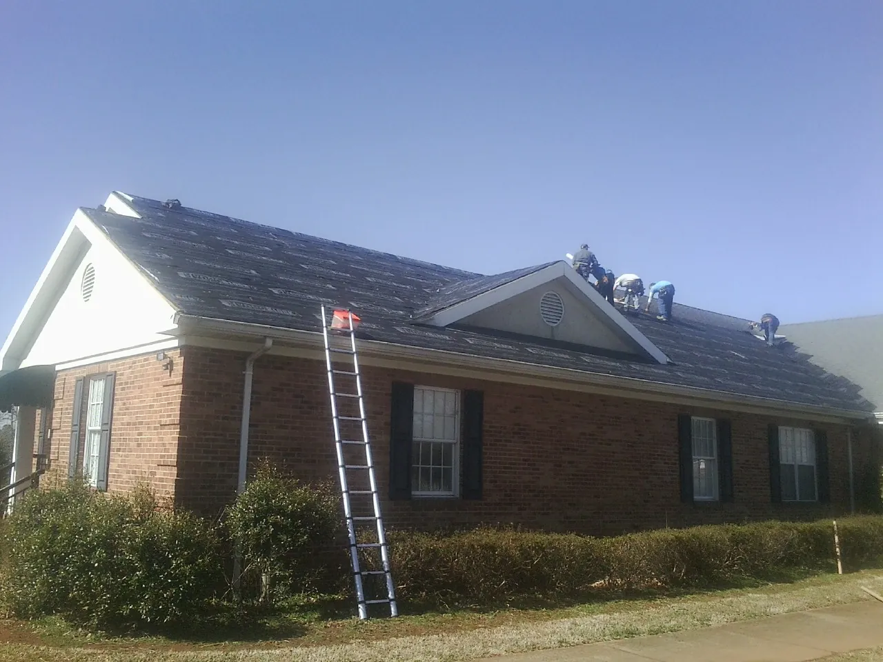 Crew tearing shingles off a brick ranch roof with a ladder set — Metal Roof Repair work by our crew in Brazil