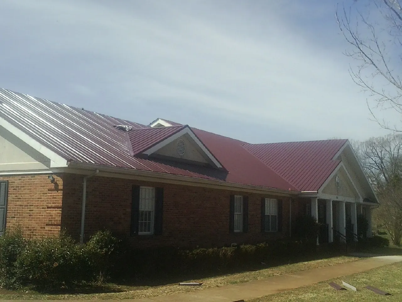Red metal roof with gabled entries on a long brick building, from a Hail Damage Roof Repair job in Brazil