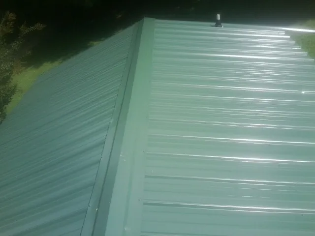 New green metal panels meeting at the ridge of a roof — Flat Roof Repair work by our crew in Brazil